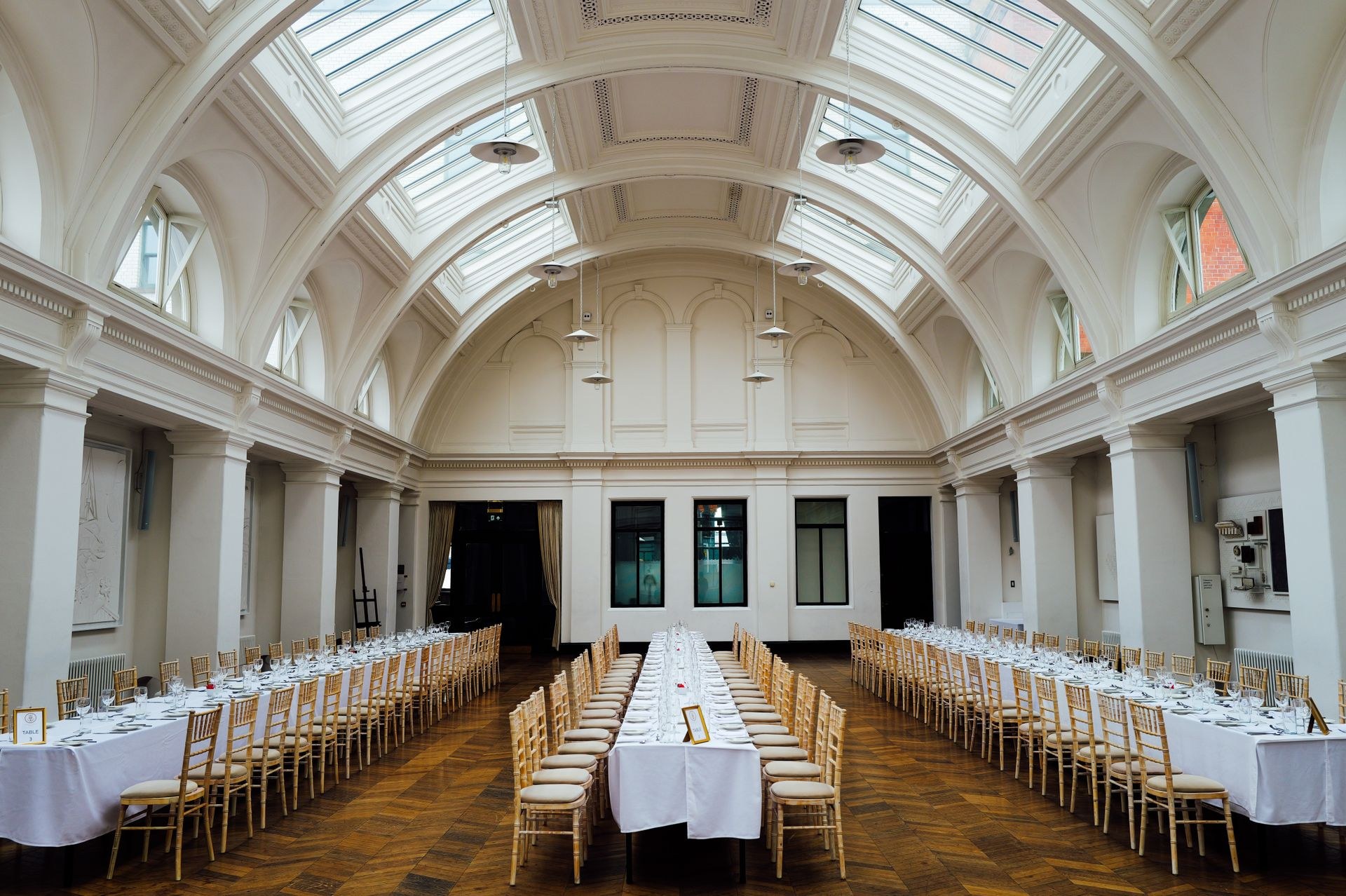 Longues tables dressées dans une salle de réception claire sous des verrières